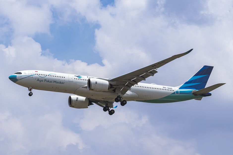 penumpang di bandara dengan latar belakang pesawat Garuda Indonesia