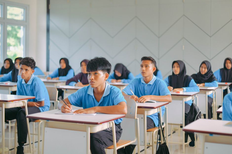 Ilustrasi guru dan siswa di sekolah, dengan komputer dan perangkat teknologi di sekitar mereka
